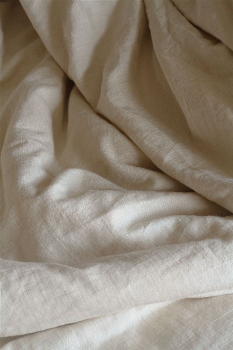 Close-up of soft, folded beige linen fabric with natural creases and gentle shadow.