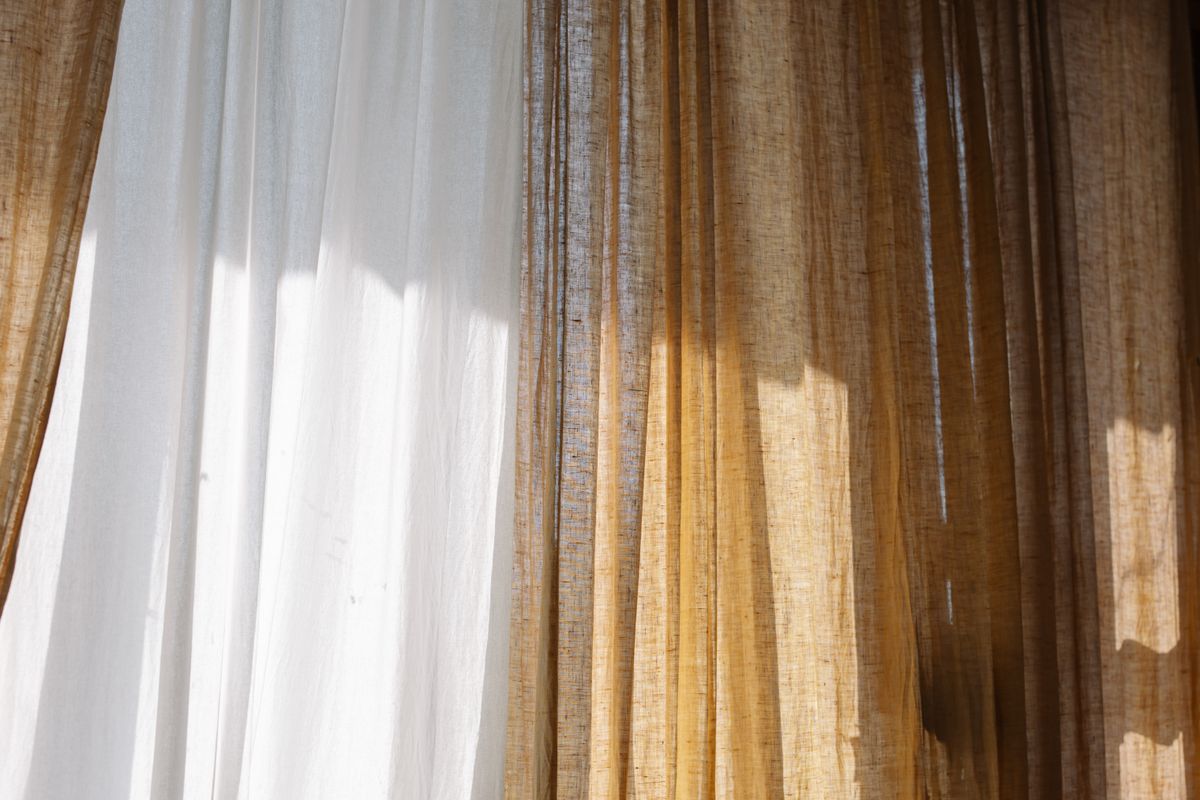 Warm sunlight streaming through sheer white and warm-toned linen curtains, close-up on the fabric and light.